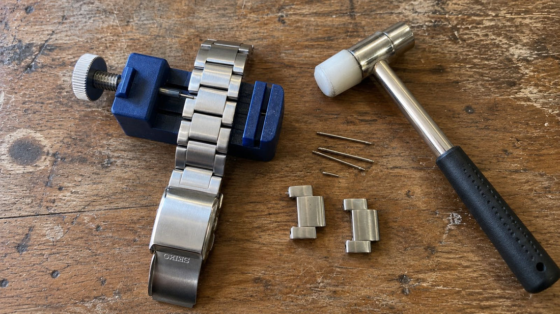 Verktyg för att korta klockarmband själv: länkverktyg, hammare, stift och borttagna länkar från ett stålklockarmband